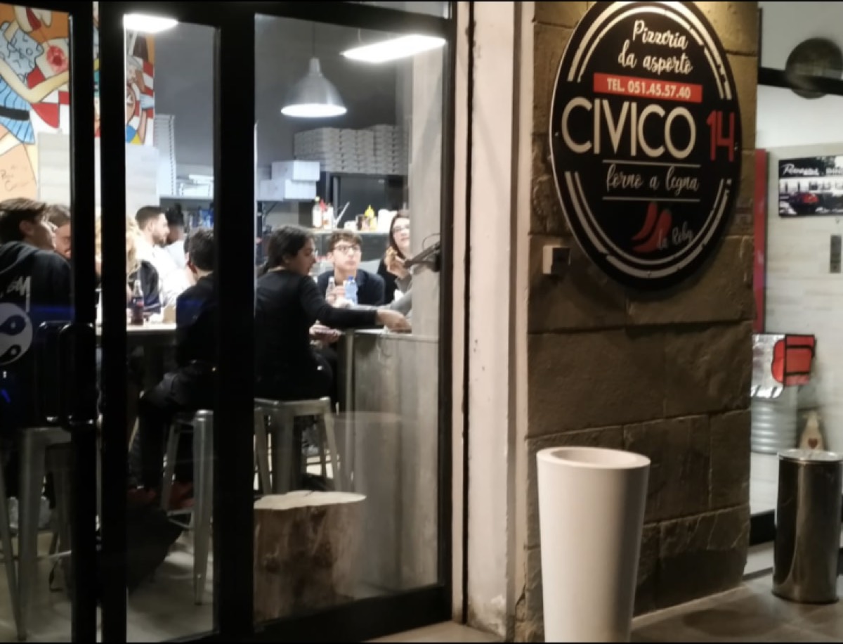 La facciata di Pizzeria Civico 14 di sera, con l'insegna tonda illuminata